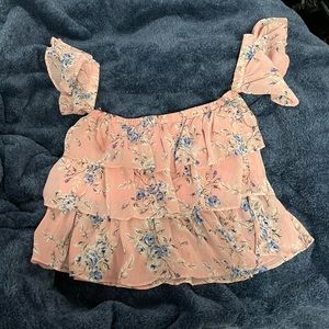 A pink off the shoulder top with frills made with a flowery material.